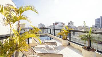 Terraço no telhado com piscina, espreguiçadeiras e plantas em vasos.