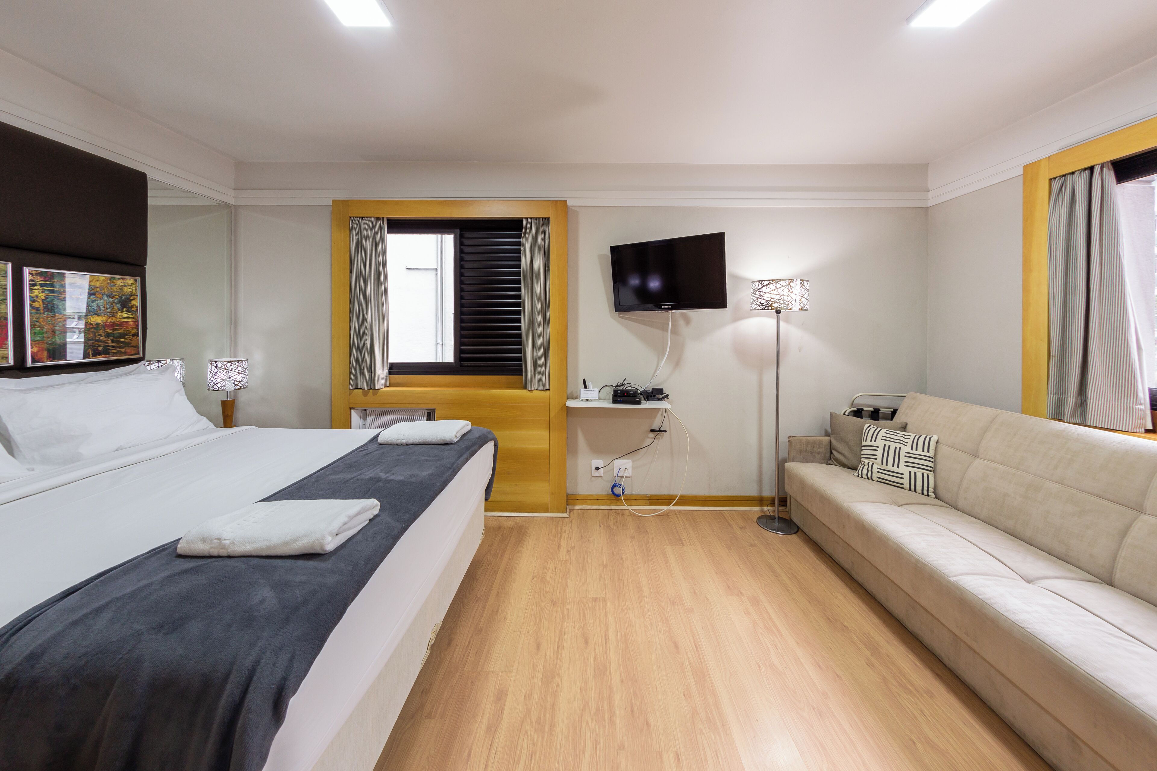 A hotel room with a bed, a sofa, a TV, and a window with blinds.