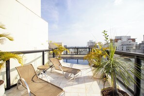 Een terras op het dak met twee lounge stoelen, een zwembadje en plantenpotten.
