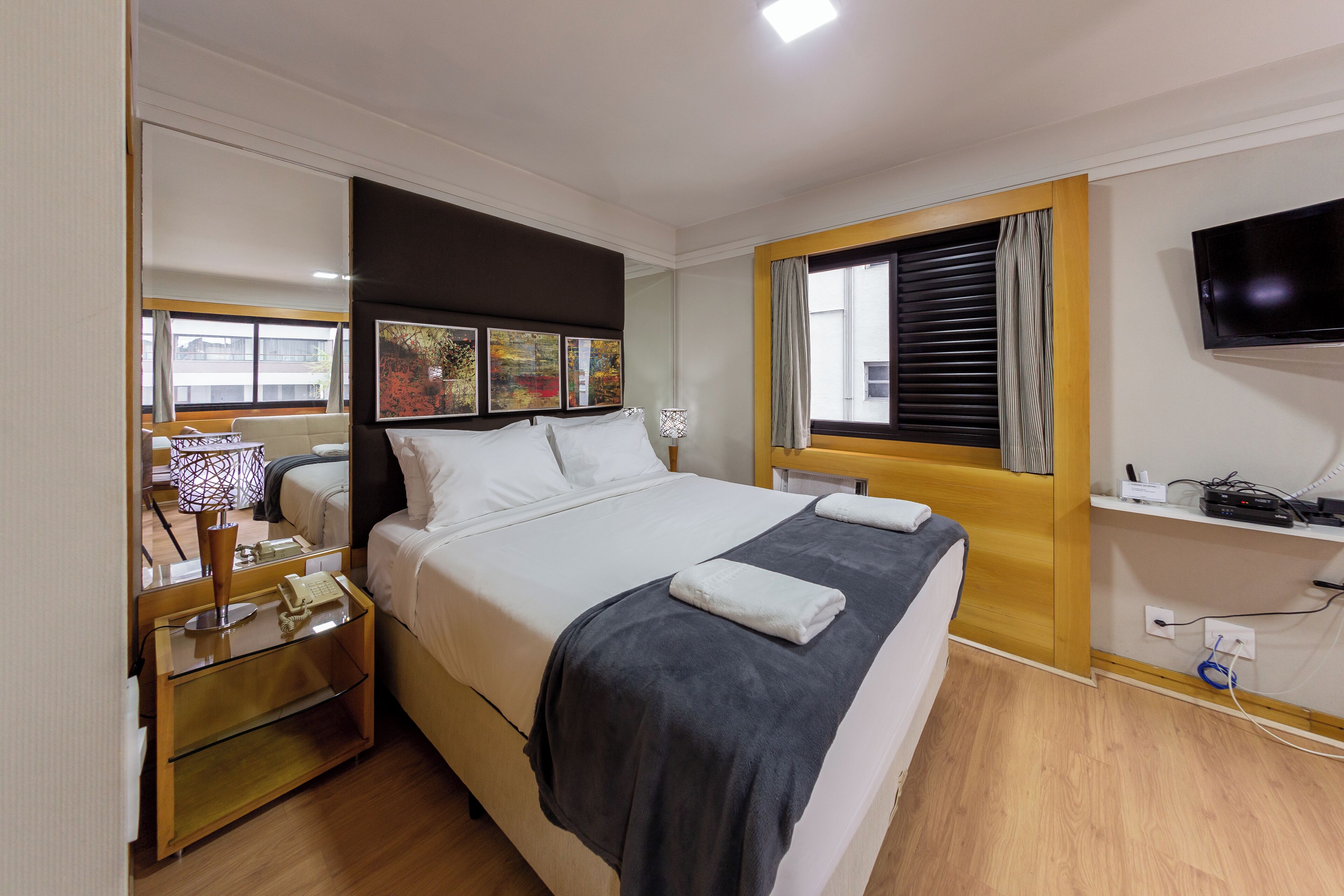 A hotel room with a bed, bedside table, lamp, and a TV mounted on the wall.