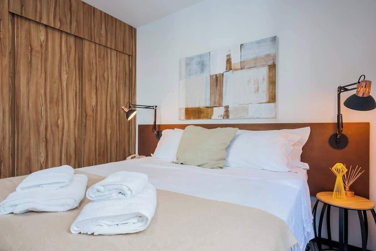 Habitación de hotel con cama, dos lámparas de noche, una obra de arte en la pared y una mesita con un objeto decorativo.