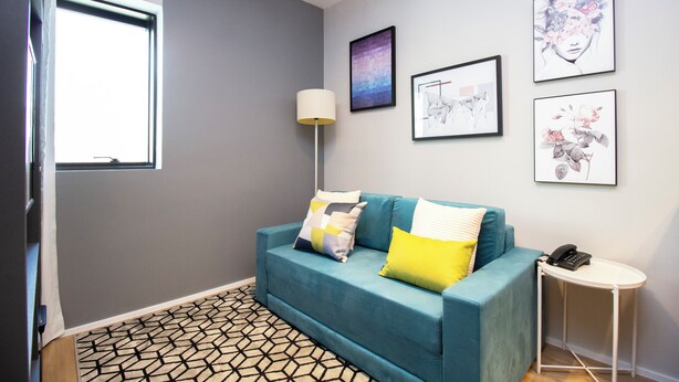 A modern living room with a teal sofa, patterned rug, and a small side table with a phone. - Advance by Bhomy (São Paulo)