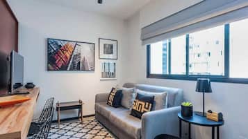 Uma sala de estar moderna com um sofá, uma mesa pequena, uma TV e obras de arte na parede.