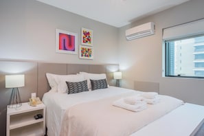 A hotel room with a bed, bedside lamps, a nightstand, a wall-mounted air conditioner, and artwork. - Advance by Bhomy (São Paulo)