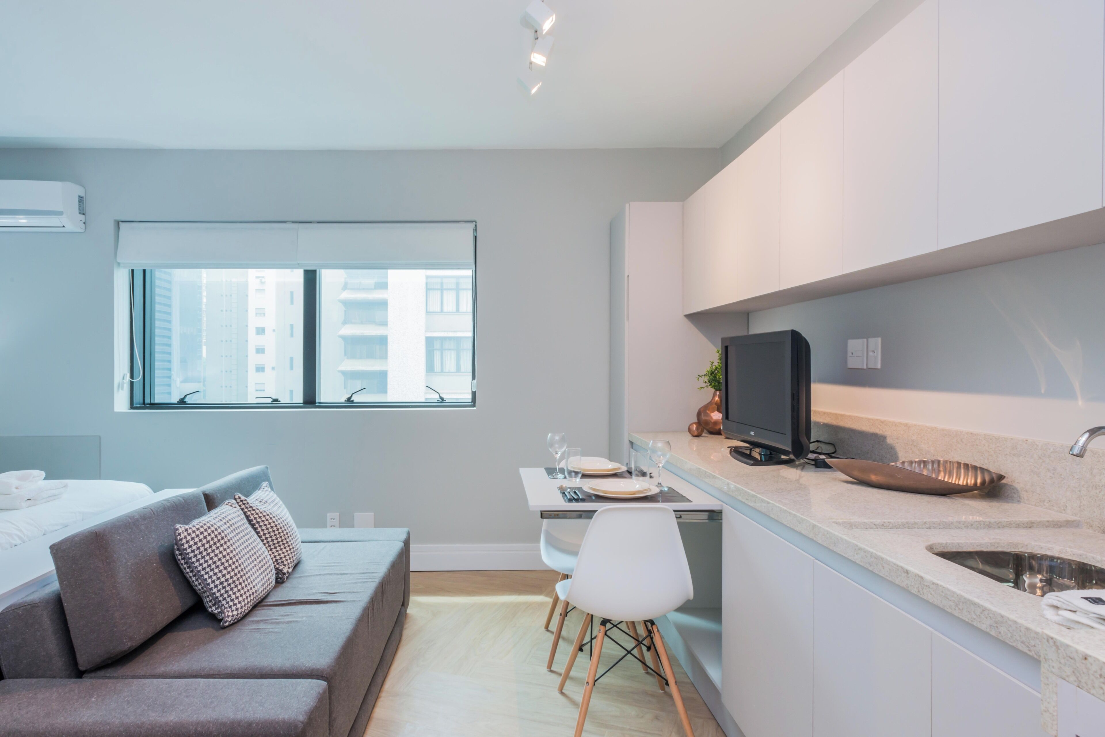 Um apartamento moderno com cozinha compacta, área de jantar e sala de estar com sofá e janela.