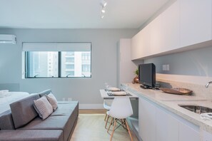 Een modern appartement met een kitchenette, een eethoek en een woonruimte met een bank en een raam.