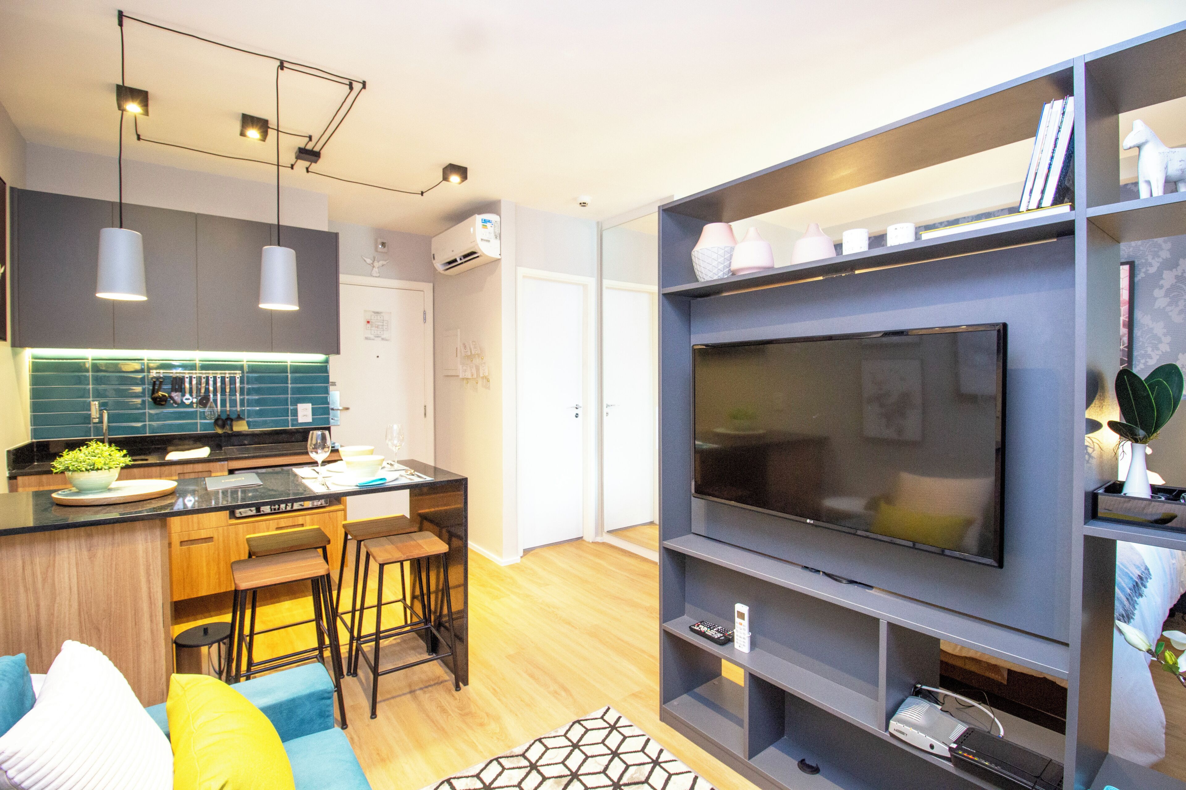 Uma sala de estar moderna com televisão de tela plana, uma área de cozinha com balcão e um espaço para refeições.