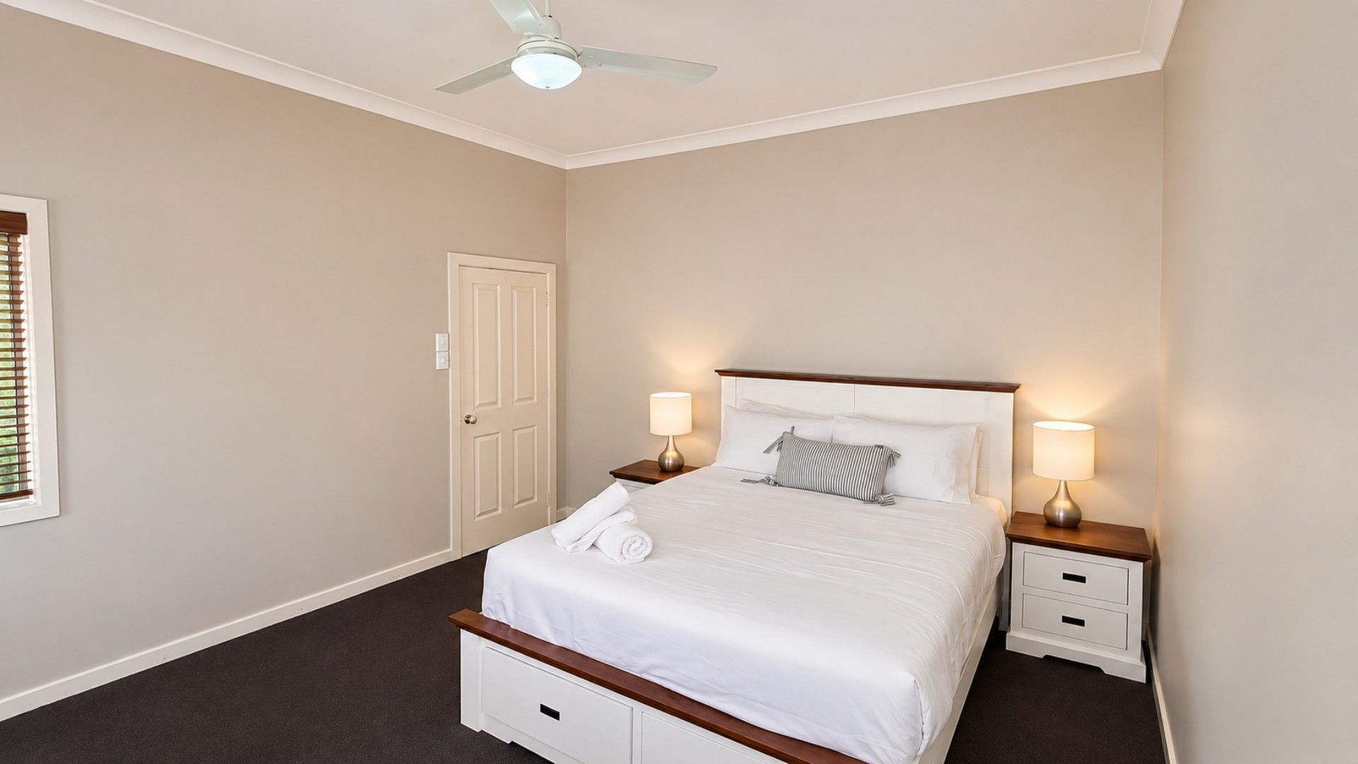 A bedroom with a bed, two bedside tables, a ceiling fan, and a door.
