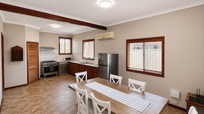 A compact kitchen with a dining area, featuring a stove, oven, microwave, refrigerator, and a window with blinds. - Rustic Charm with room for the Boat (West Busselton)