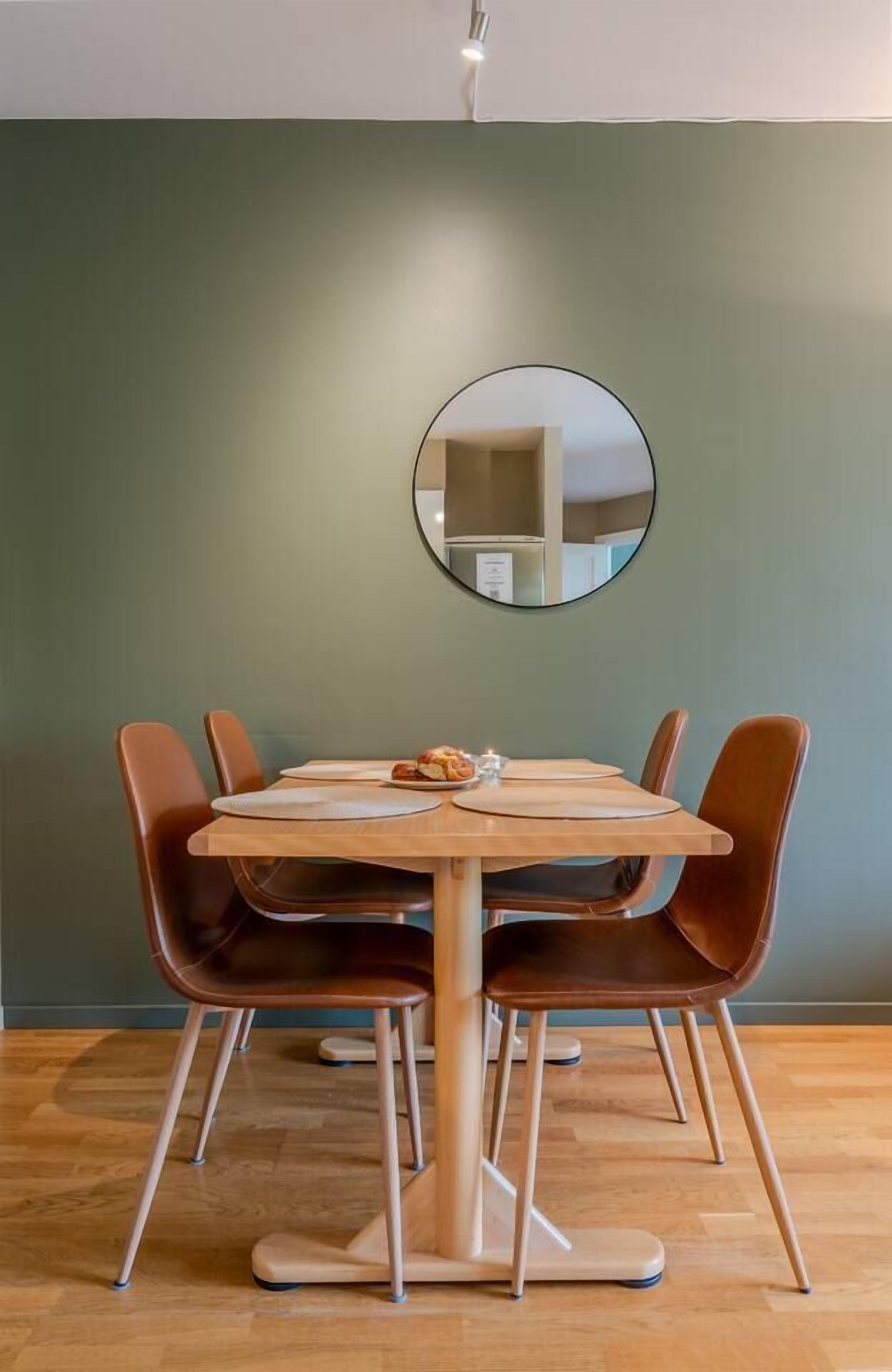 Ein Essbereich mit einem Holztisch und braunen Stühlen, einem runden Spiegel an der Wand und einer Lampe darüber.