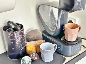 A coffee maker, a mug, a container with coffee beans, a box of biscuits, and a container with a lid.