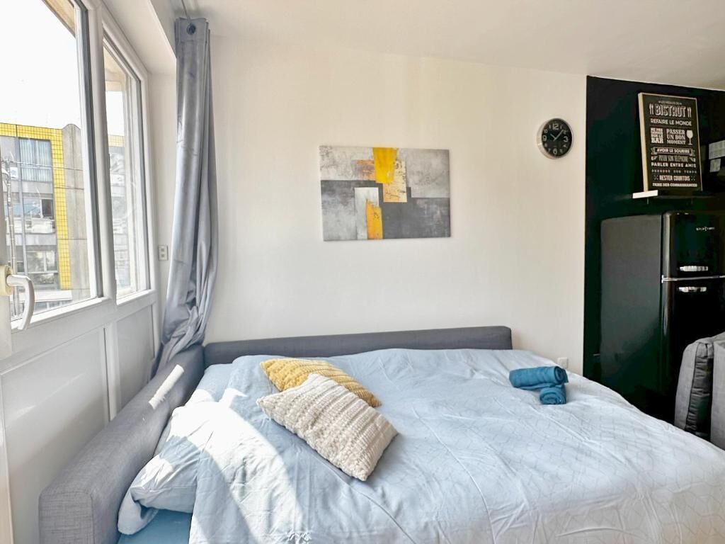 Hotellihuone, jossa on sänky, ikkuna verhoilla, seinäkello ja abstrakti taideteos.