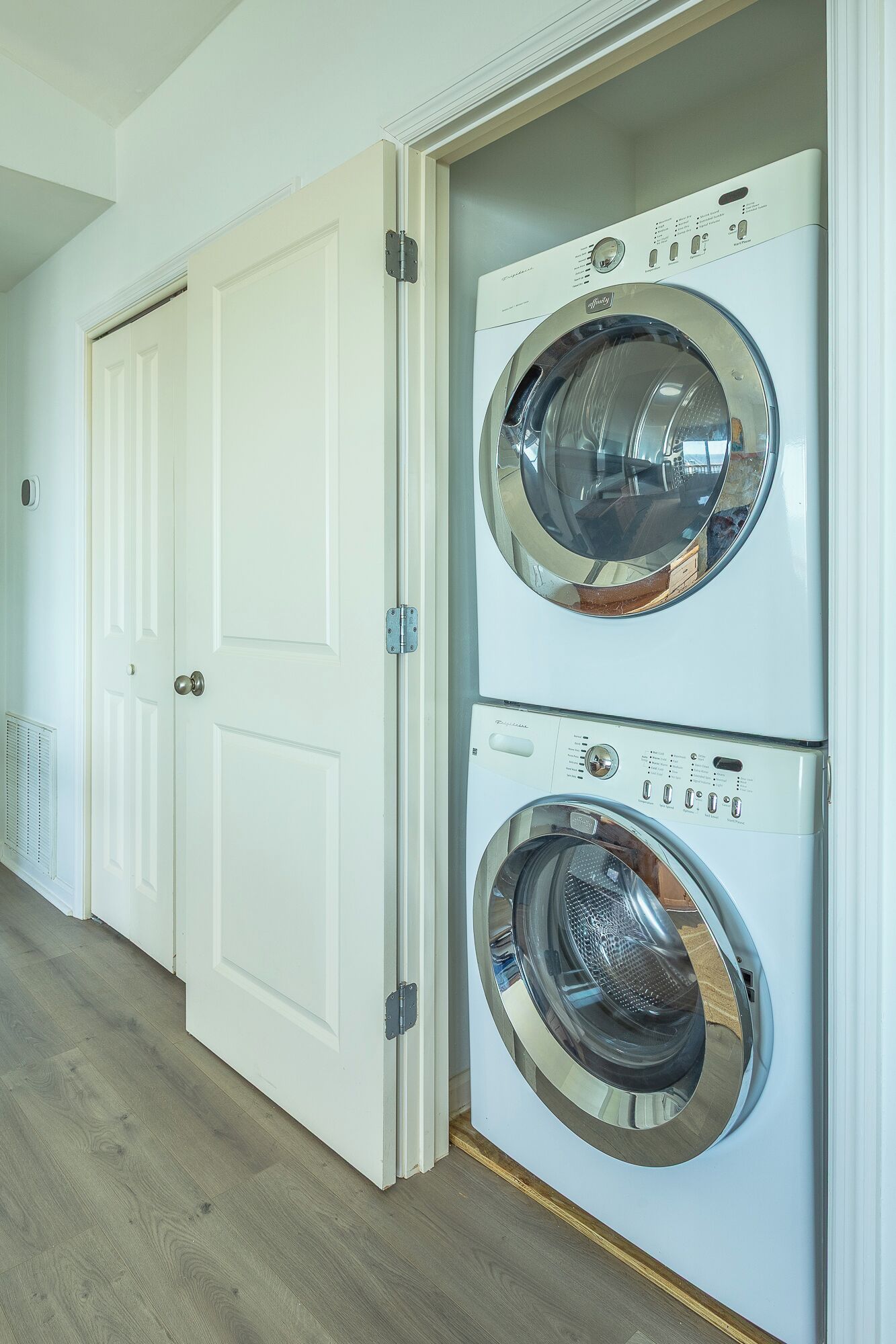A laundry room with two stacked front-loading washing machines and a white door.