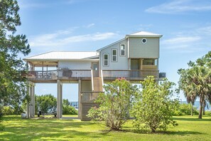 Ein zweigeschossiges Haus mit einem Balkon im oberen Bereich und einer Veranda im unteren Bereich, mit Blick auf das Wasser.