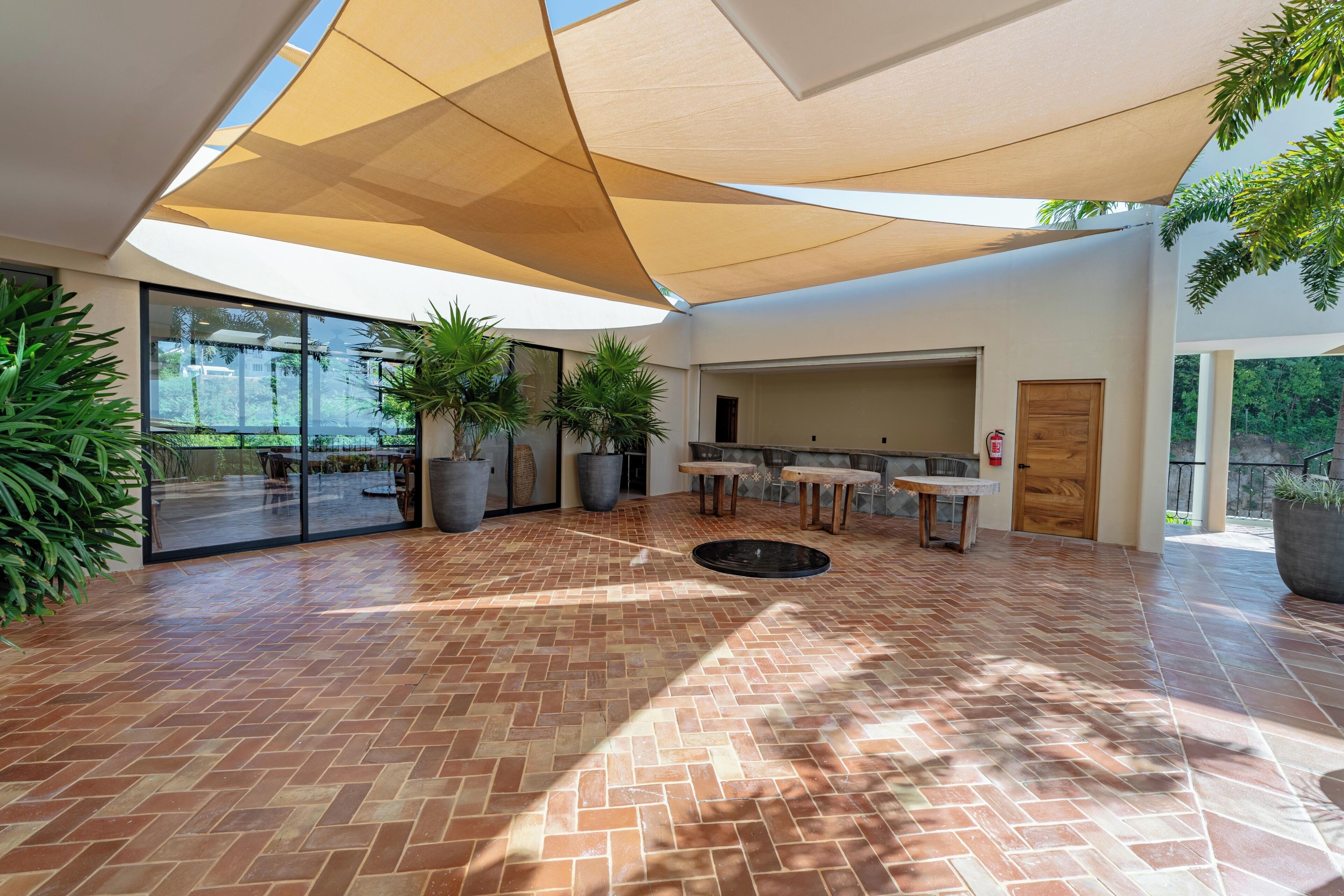 Un patio interior con suelo de baldosas, plantas grandes en macetas y un conjunto de asientos.