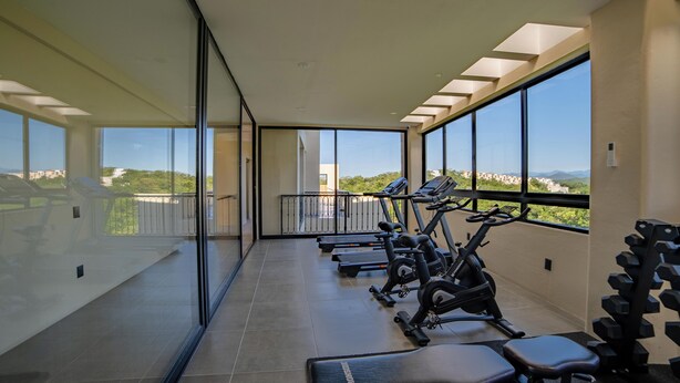 Un gimnasio con equipamiento de ejercicio y amplios ventanales que ofrecen vistas de la ciudad.