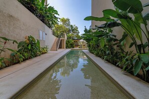 Ein Pool mit einer gefliesten Umrandung, umgeben von üppiger Vegetation und einer Treppe zu einem überdachten Bereich.