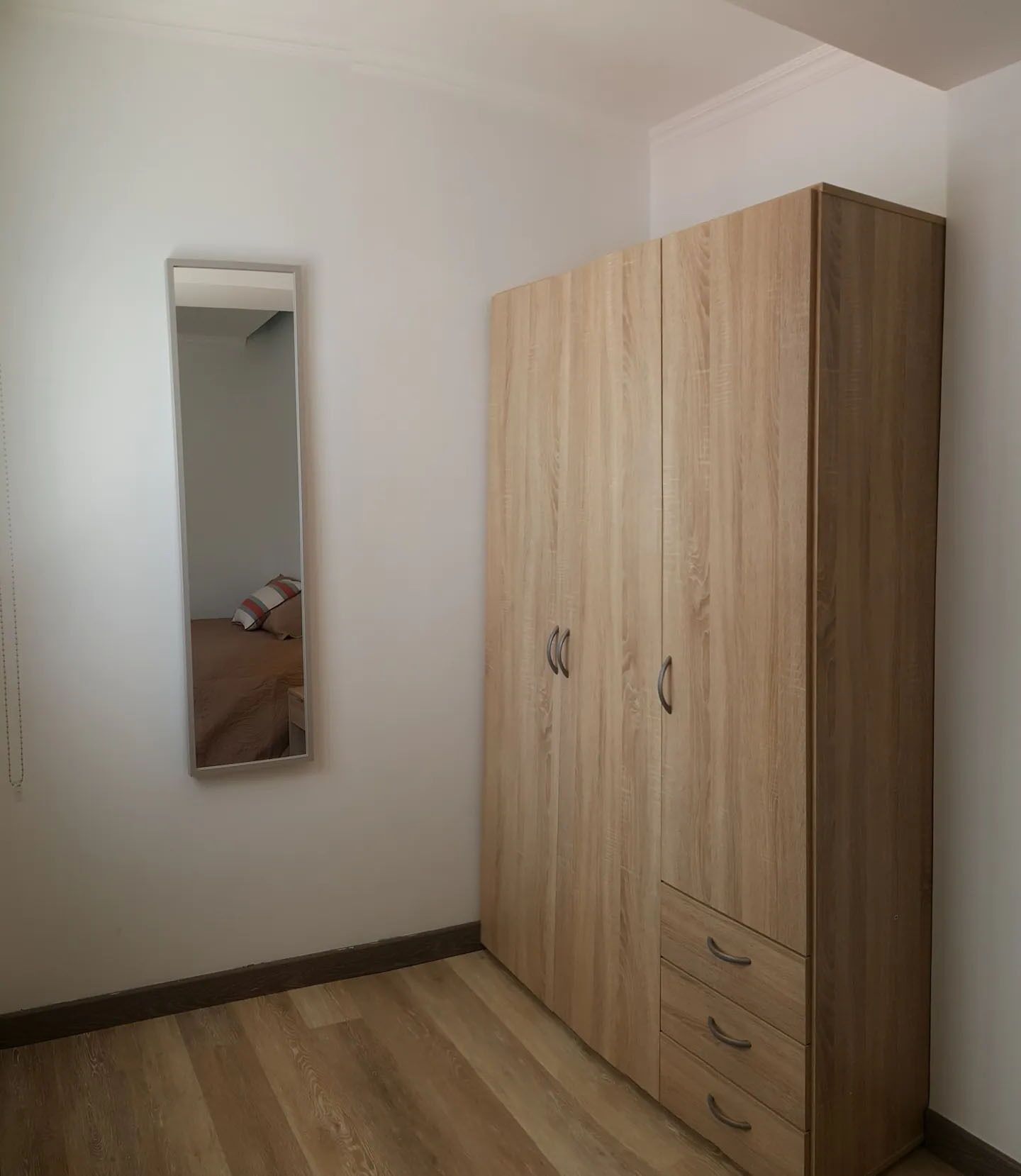 A room with a large wardrobe, a mirror, and a bed.