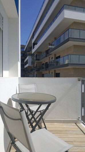 Ein Balkon mit Tisch und Stühlen, mit Blick auf ein mehrstöckiges Gebäude mit Balkonen.