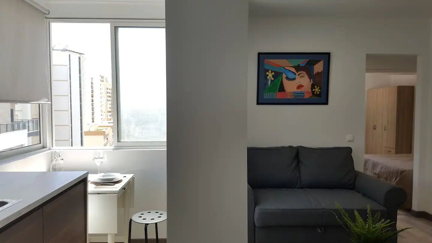A modern apartment with a kitchen, dining area, and a living room with a sofa and a painting on the wall.