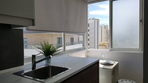 A modern kitchen with a sink, a potted plant, and a window overlooking a cityscape. - One-bedroom apartment 150 meters from Praia da Rocha (Portimão)