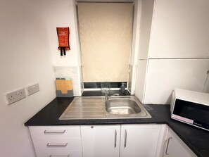 A kitchen with a black countertop, white cabinets, a stainless steel sink, a microwave, and a fire blanket on the wall. - Contractors & Families pick- Racecourse,Shopping & Attractions-Parking (Doncaster)