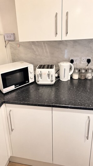 A kitchen with white cabinets, a black countertop, a microwave, a toaster, a kettle, and a coffee maker. - Contractors & Families pick- Racecourse,Shopping & Attractions-Parking (Doncaster)
