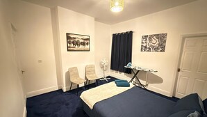 A bedroom with a bed, chairs, an ironing board, and artwork on the walls. - Spacious 3BR Doncaster Home Near Racecourse, Shopping & Attractions (Doncaster)