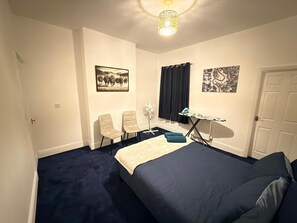 Een slaapkamer met een bed, stoelen, een strijkplank en kunst aan de muren.