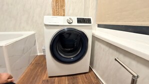 A front-loading washing machine in a bathroom with a wooden floor and a window with a towel rack. - Spacious 3BR Doncaster Home Near Racecourse, Shopping & Attractions (Doncaster)