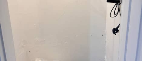 A small, narrow room with a single bed, a white wall, and a door.