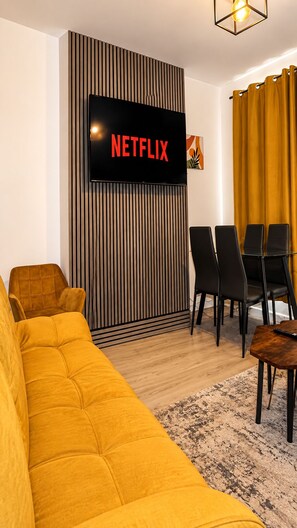 A modern living room with a large flat-screen TV mounted on a wall, a yellow sofa, a dining table with chairs, and a patterned rug. - Contractors & Families pick- Racecourse,Shopping & Attractions-Parking (Doncaster)