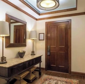 Une pièce avec une porte en bois, un miroir, une coiffeuse avec une lampe et un tapis à motifs.
