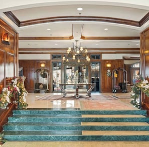 A grand lobby with marble stairs, a chandelier, and wooden paneling.
