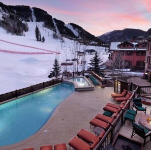 Ein Poolbereich mit Liegestühlen, einem Pool und Blick auf eine verschneite Berglandschaft.