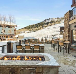 Eine Terrassensitzgelegenheit mit Steinmöbeln und Feuerstelle, mit Blick auf eine verschneite Landschaft.