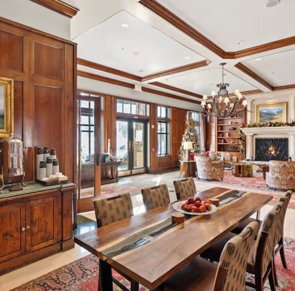 A spacious room with a large wooden dining table, comfortable seating, a fireplace, and a bookshelf.