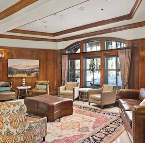 A spacious living room with leather sofas, a patterned rug, and large windows with curtains.