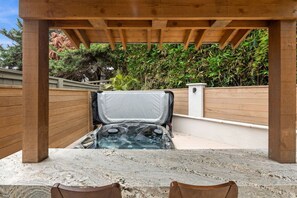 A hot tub under a wooden pergola with a stone floor, surrounded by a wooden fence and greenery. - Beacons Beach Retreat | Steps from the Sand (Encinitas)