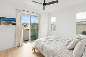 A bedroom with a bed, a ceiling fan, a balcony door, and a window. - Beacons Beach Retreat | Steps from the Sand (Encinitas)