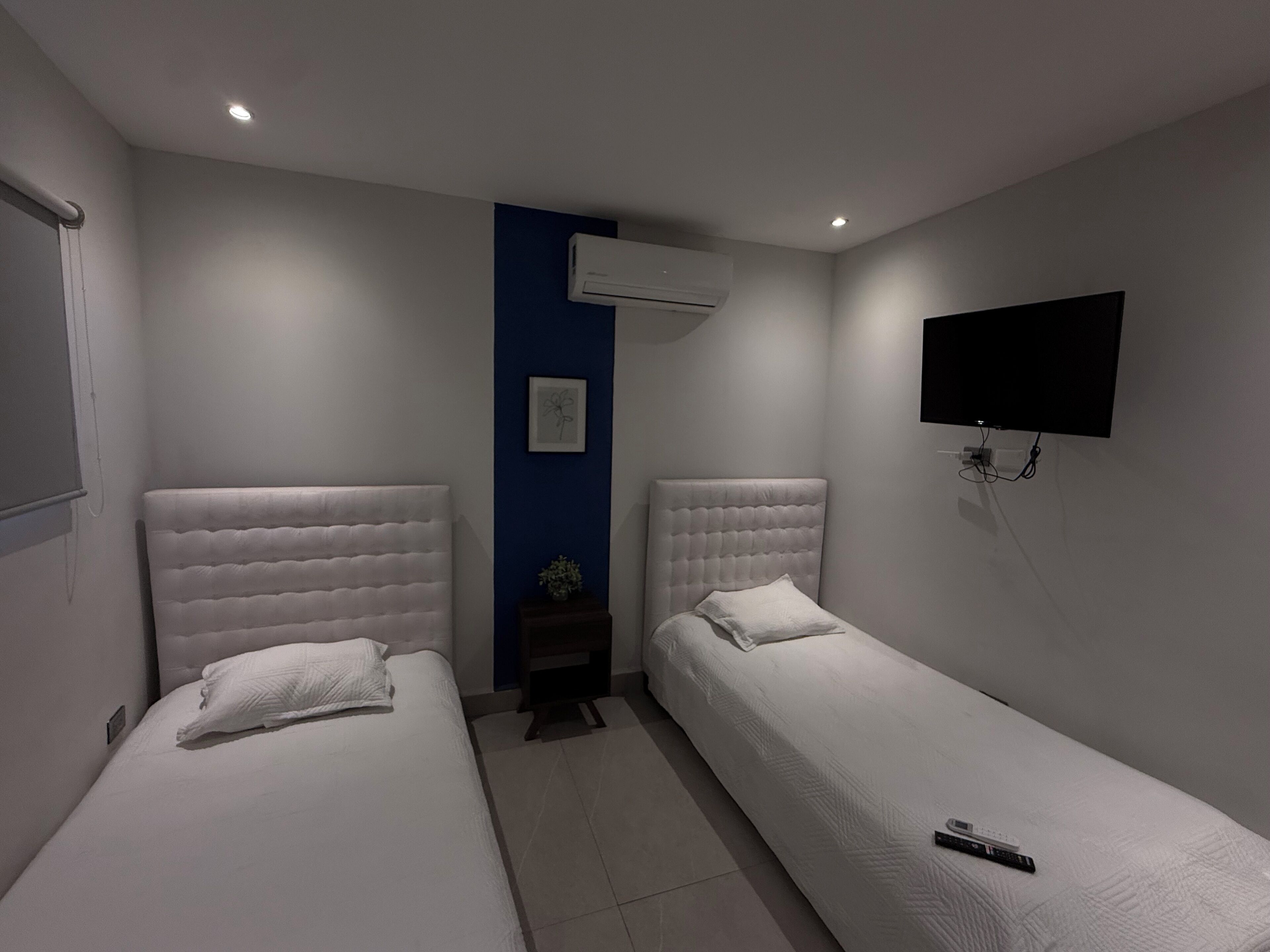 A hotel room with two beds, a wall-mounted TV, and an air conditioning unit.