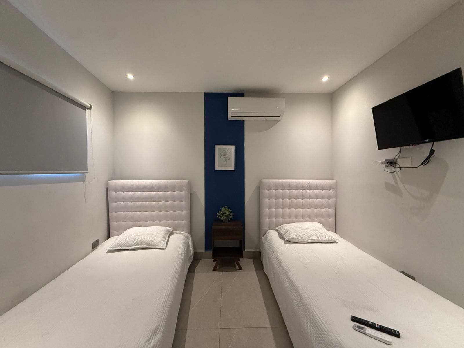 Quarto de hotel com duas camas, uma TV fixada na parede e um ar condicionado.