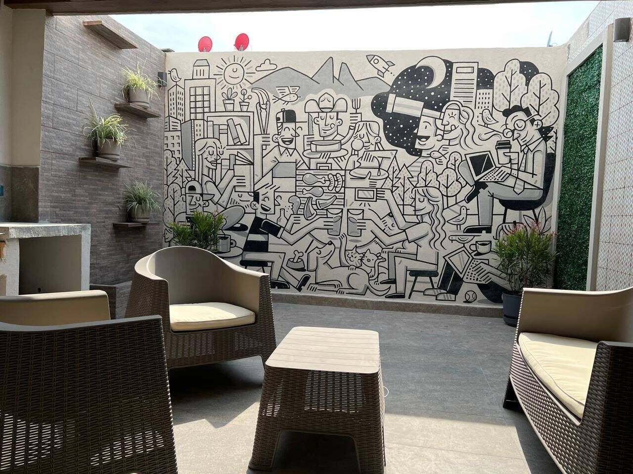Un área de estar al aire libre con mobiliario de mimbre y una pared mural.