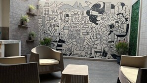 Un área de estar al aire libre con mobiliario de mimbre y una pared mural.