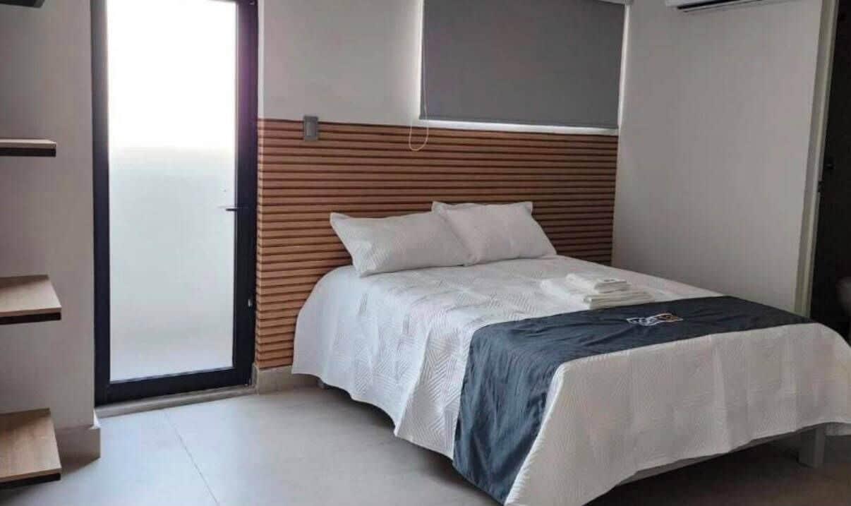 Un dormitorio con una cama, un cabecero de madera, una pared blanca y una puerta que da a un balcón.