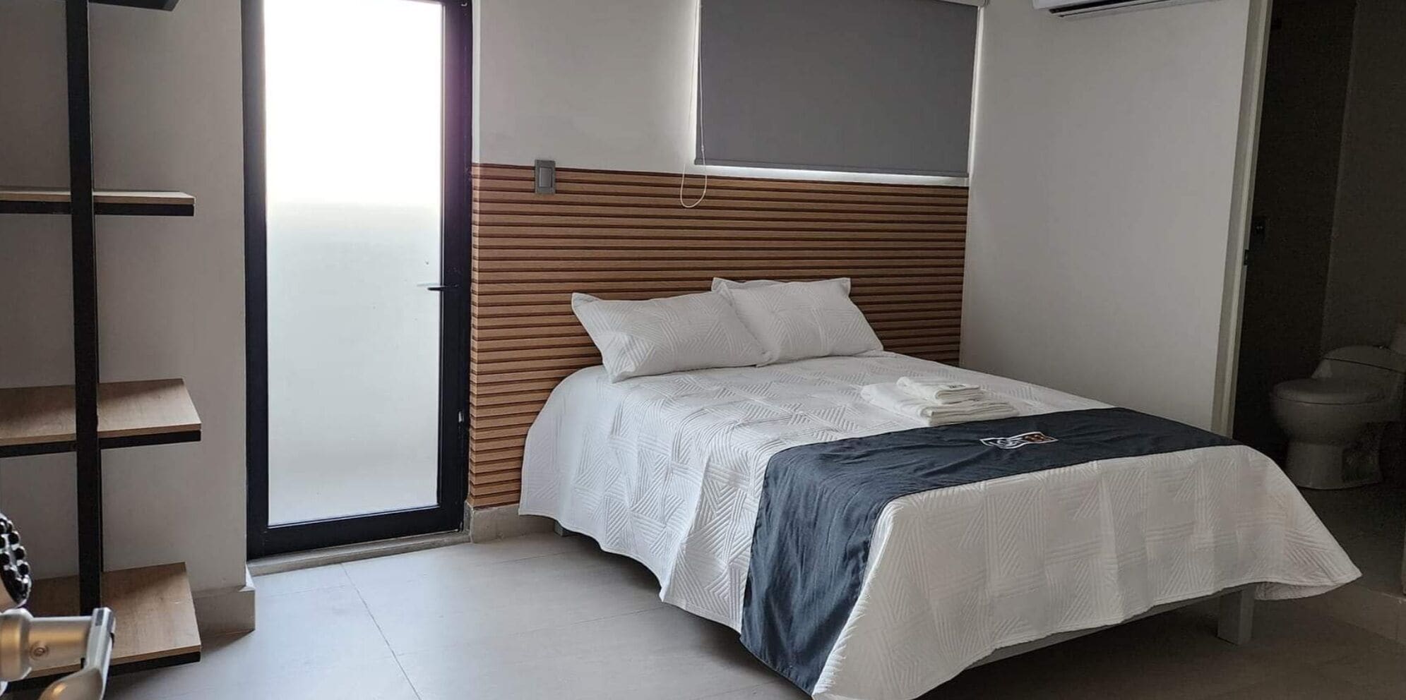 Un dormitorio con cama, cabecero de madera, ventana y un inodoro.
