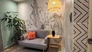 Una sala moderna con un sofá gris, una mesita de madera, una lámpara de pared y una planta grande en maceta.