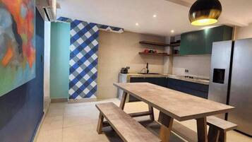 A modern kitchen with a wooden table and bench, a refrigerator, and a pendant light.