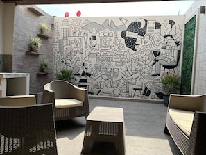 An outdoor seating area with wicker furniture and a mural wall. - Loft 33 (Monterrey)