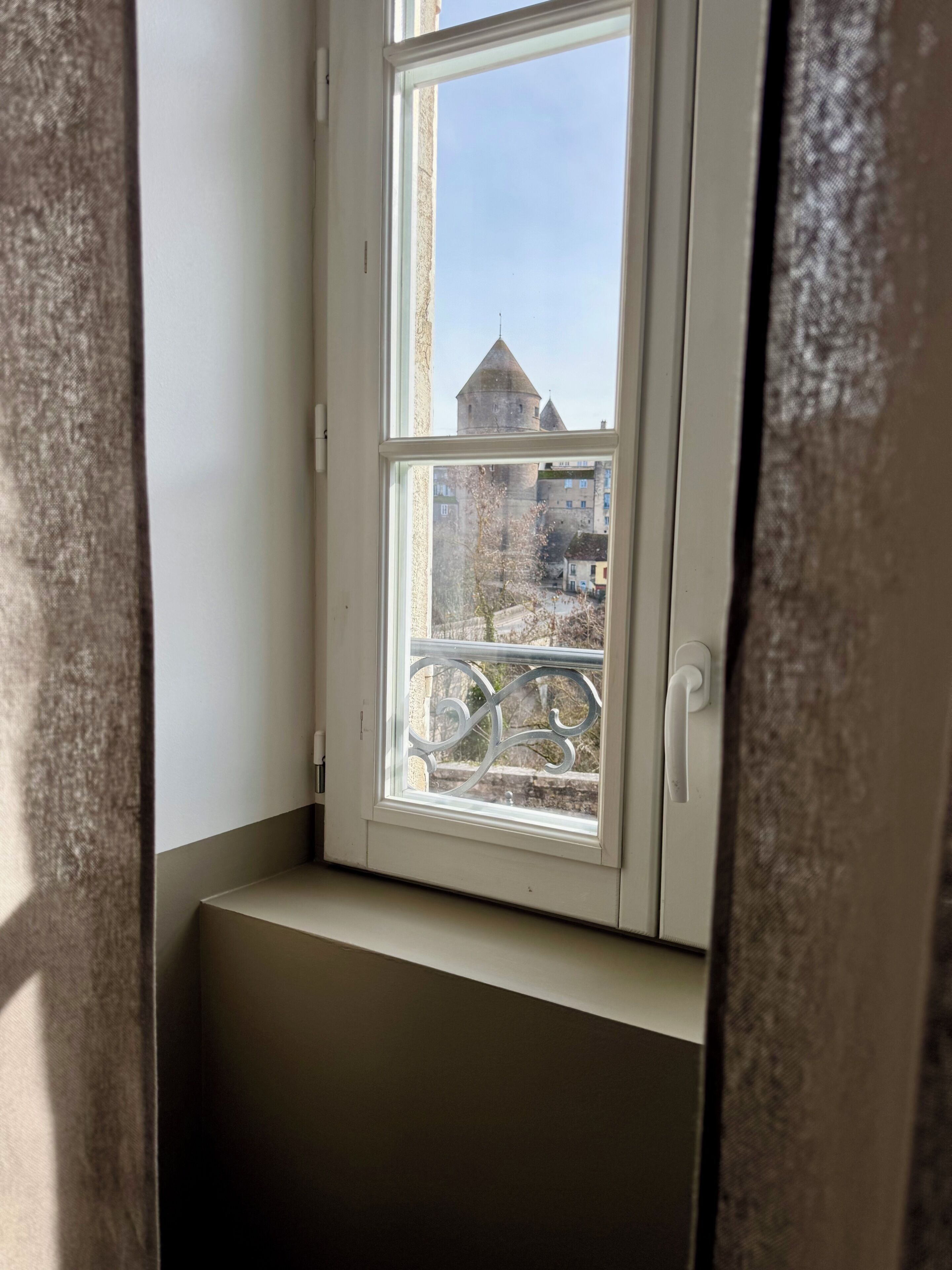 A window with a view of a building with a tower, a balcony, and a door.